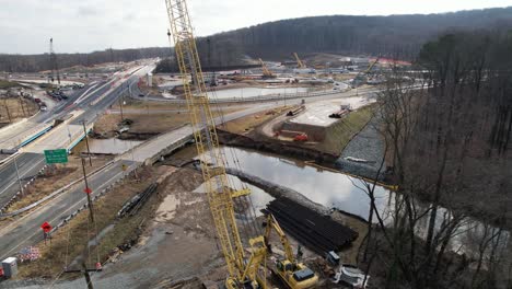 Reverse-drone-past-crane-construction-site-on-highway-in-winter-Delaware