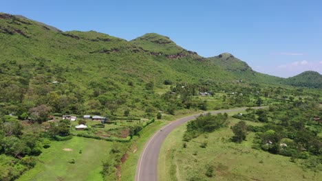 A-drone-shot-of-beautiful-green-farmlands-with-hills-on-one-side-and-a-road-in-the-middle-of-the-frame