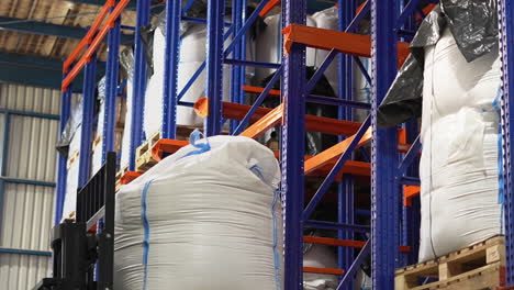 A-mechanized-forklift-is-lifting-a-heavy-white-bag-to-a-top-shelf-in-a-fully-loaded-warehouse