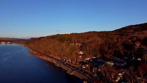 Golden-hour-aerial-view-of-a-serene-lakeside-with-train-tracks-and-dense-woodland