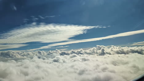 Window-view-of-an-airplane-flying-over-white-clouds-under-a-blue-heaven