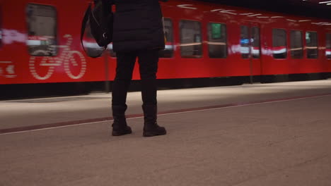 Woman-steps-to-center-as-red-subway-train-arrives-at-station,-Helsinki