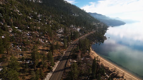 Drone-Shot-of-Coastal-Road,-Forest-and-Beach-on-Lake-Tahoe-USA-on-Sunny-Winter-Day