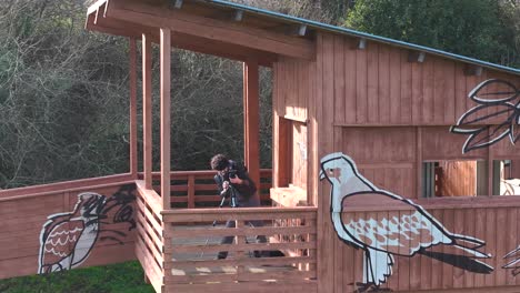 Reisefotograf,-Der-Seine-Kamera-Auf-Einem-Stativ-Auf-Dem-Balkon-Einer-Holzhütte-Im-Wald-Aufstellt