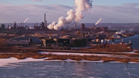 Winter-industrial-landscape-with-smokestacks-and-frozen-river,-late-afternoon-light,-wide-shot