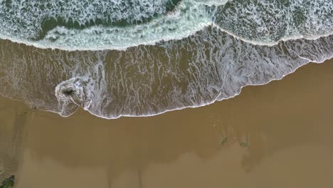 Top-View-Of-Foamy-Ocean-Waves-Washing-Beach---Drone-Shot,-Slow-Motion