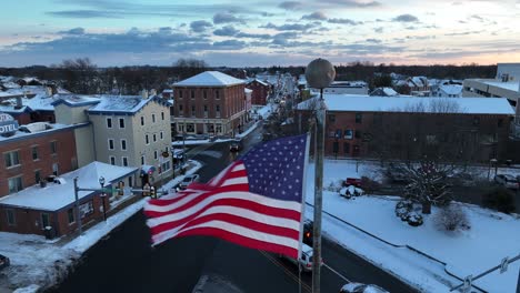 Close-up-drone-shot-of-American-flag-blowing-over-snowy-American-city-at-Christmas