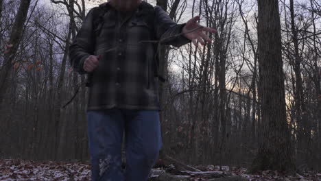 slow-motion-shot-of-a-man-with-a-big-red-beard-wearing-outdoor-gear-walking-through-the-forest-in-winter-breaking-branches-collecting-fire-wood-for-a-campfire