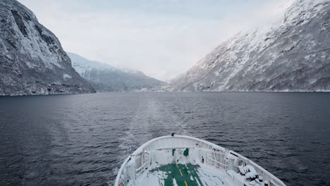 Slow-motion-POV-of-a-winter-ferry-boat-ride-in-Geirangerfjord-to-Geiranger,-Norway,-with-snowy-mountains-and-captivating-fjord-views