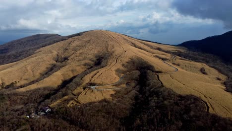 Winding-roads-on-a-barren-hillside-with-patches-of-trees-under-a-cloudy-sky,-late-afternoon,-aerial-view