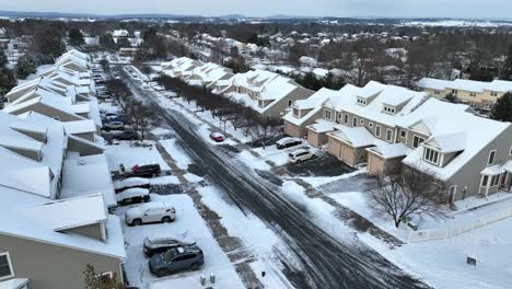 Snowy-neighborhood-with-uniform-houses-and-parked-cars-along-a-cleared-street