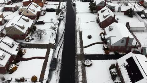 An-aerial-view-over-a-quiet,-suburban-neighborhood-after-a-snow-storm-with-the-area-covered-with-snow-on-a-cloudy-day