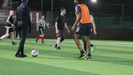 Football-players-play-soccer-outdoors-at-night-on-an-illuminated-green-field-with-artificial-grass