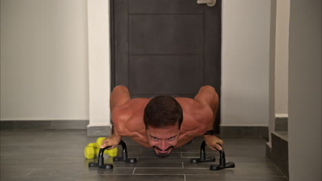 Vista-Frontal-En-Cámara-Lenta-De-Un-Hombre-Latino-Hispano-En-Forma-Entrenando-En-Casa-Haciendo-Flexiones-Usando-Barras-De-Soporte-De-Ayuda