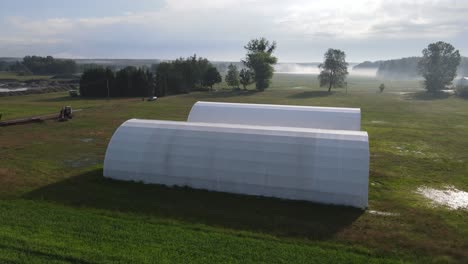 two-white-arched-hall-warehouse-on-farm-aerial-in-sunny-morning-day