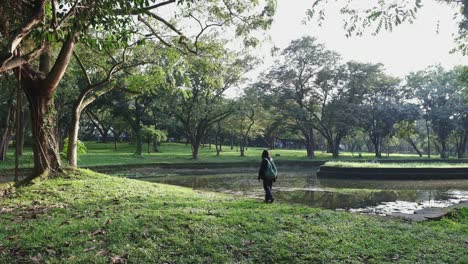 Young-Woman-With-Backpack-Walking-Alone-On-A-Peaceful-Park-With-Pond