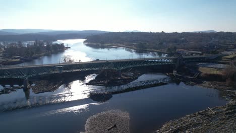 Side-tracking-along-historic-New-England-bridge-over-dams-and-waterways-with-early-sunlight-shimmering-and-a-rocky-riverbed-in-foreground