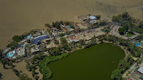 Aerial-Shot-Over-Huacachina-Oasis-Lake-Surrounded-by-Sand-Dunes-in-Atacama-Desert,-Peru