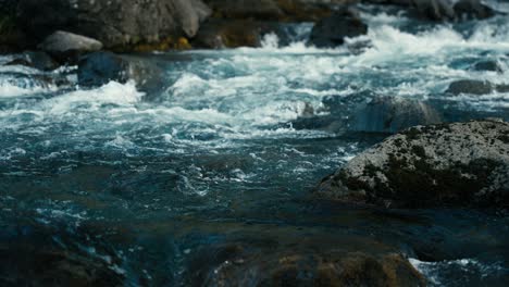 Close-up-of-crystal-clear-blue-water-flowing-down-a-river-and-splashing-over-rocks