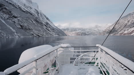 Slow-motion-POV-of-a-winter-ferry-boat-ride-in-Geirangerfjord-to-Geiranger,-Norway,-with-snowy-mountains-and-captivating-fjord-views