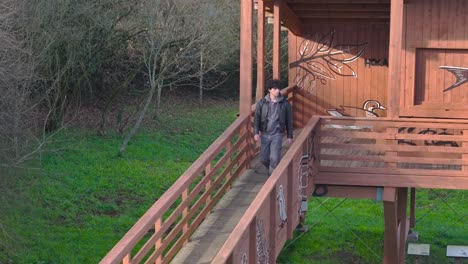 Young-European-Man-Walking-Out-Of-Wooden-Cabin-In-The-Forest-On-Sunny-Day-In-Spain