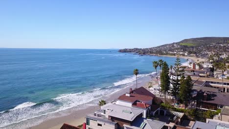 Breathtaking-Aerial-Shot-of-Laguna-Beach,-California-Beachfront-Homes-Overlooking-the-Crystal-Clear-Pacific-Ocean-on-a-Sunny-Day