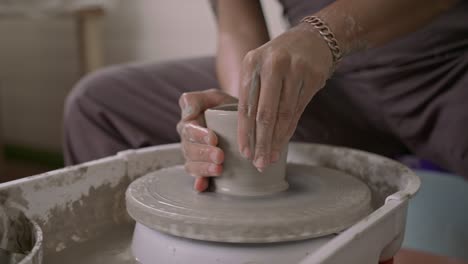 Craftsperson-shaping-pottery-on-a-wheel,-hands-detailed-in-clay