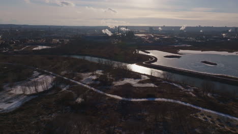 Meandering-river-with-industrial-backdrop,-winter-tones,-late-afternoon-light,-aerial-view