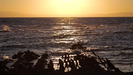 Wunderschöner-Blick-Auf-Den-Sonnenuntergang-Von-Den-Silhouetten-Der-Klippen-Mit-Der-Sonne,-Die-In-Zeitlupe-Im-Meer-Glitzert