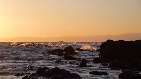 Slow-motion-scenery-of-waves-breaking-against-silhouette-rocks-during-vibrant-sunset