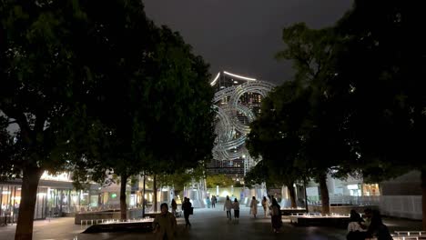 Nachtansicht-Eines-Stadtparks-Mit-Beleuchteter-Kunstinstallation,-Flanierenden-Menschen,-Bäumen,-Die-Die-Szene-Einrahmen,-In-Yokohama,-Japan