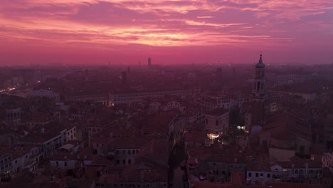 Venice-at-dusk-with-pink-hued-sky-and-city-lights-beginning-to-glow,-aerial-view