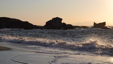 Wunderschöne-Wellen,-Die-In-Zeitlupe-An-Einem-Weiten-Strand-Mit-Felssilhouetten-Brechen