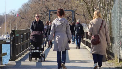 Women-walk-over-wooden-bridge-on-sunny-day-in-Stockholm,-one-rolls-stroller