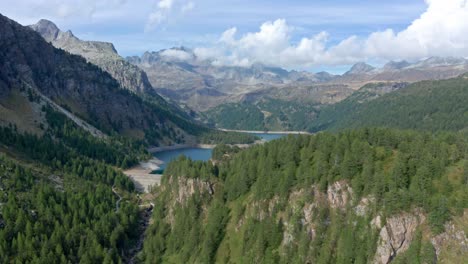 Lago-di-devero-in-alpe-devero-with-lush-forests-and-rugged-mountains,-aerial-view