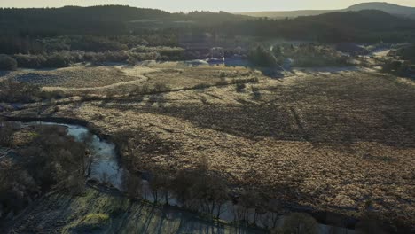 Late-Afternoon-Sunlight-Casting-Shadows-Across-an-Empty-Field-with-an-Aerial-Drone-Panning-Shot-at-Aberfoyle-Village-in-Scotland