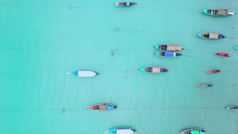 Aerial-Top-Down-Shot-Over-Wooden-Huts-Along-a-Beach-with-Long-Tail-Boats-in-Turquoise-Waters-in-Thailand