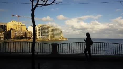 POV-Malta-sidewalk-view-across-seascape-to-hotel-building-along-coastline-seascape