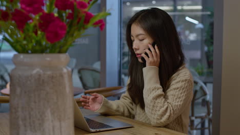 Junges-Asiatisches-Mädchen-Telefoniert-Aktiv-Vor-Ihrem-Laptop,-Während-Sie-Von-Einem-Café-Aus-Arbeitet