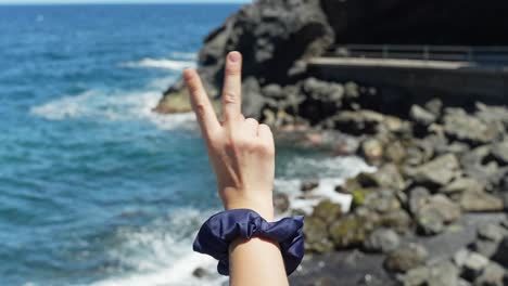 Weibliche-Hand-Hält-Friedenszeichen-Mit-Fingern-Auf-Tropischem-Meeresküstenhintergrund