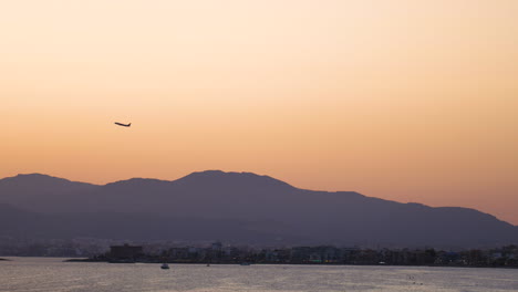 Silueta-De-Avión-Despegando-Sobre-La-Brumosa-Cordillera-De-Mallorca-A-Través-Del-Horizonte-Naranja-Dorado