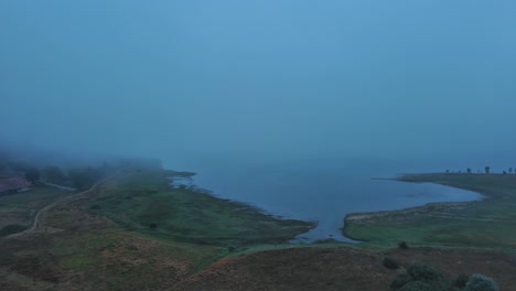 Misty-dawn-over-Nanclares-de-Gamboa-with-a-serene-lake-and-sleepy-village,-Basque-Country,-Spain,-aerial-view