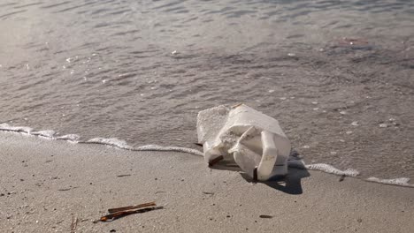 Botella-De-Plástico-Desechada-En-La-Playa-De-Arena-Con-Suaves-Olas-En-El-Fondo,-Cuestión-Ambiental