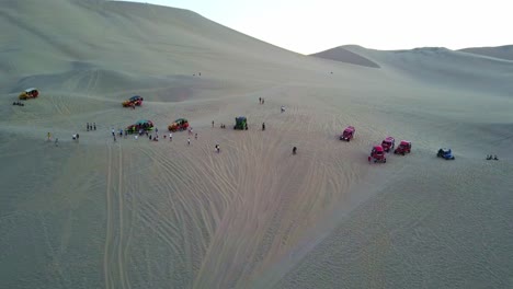 Desert-Buggies-Parked-on-top-of-a-Sand-Dune-at-Huacachina-Oasis-with-an-Aerial-Drone-Shot-Tilting-Up,-Peru,-South-America
