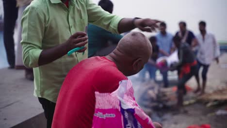 Side-angle-view-of-a-local-barber-cutting-hair-at-Varanasi-burning-ghat-during-evening-in-India