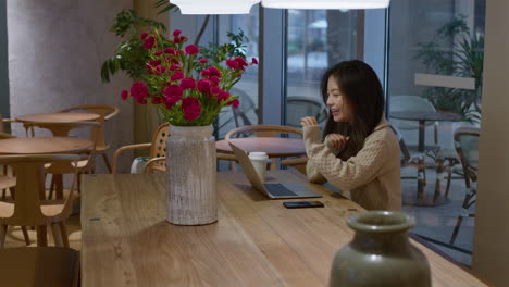 Young-pretty-asian-Chinese-girl-talks-happily-and-smiles-during-online-call-in-cafe