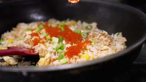Chef-sprinkles-masago-fish-roe-over-freshly-made-crab-fried-rice-in-skillet,-close-up-slow-motion-4K