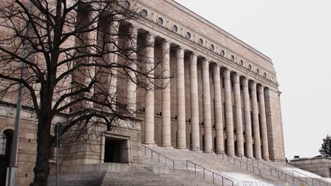 Tree-branches-framing-the-imposing-facade-of-Helsinki's-Parliament-House,-overcast-sky
