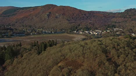 Luftaufnahme-Mit-Einem-Schwenk-über-Den-Bewaldeten-Hügel-Im-Dorf-Aberfoyle-Mit-Craigmore-Im-Hintergrund,-Schottland