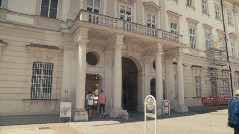 Sunny-day-in-Salzburg,-view-of-pedestrians-walking-by-a-historic-European-building-with-columns,-static-shot